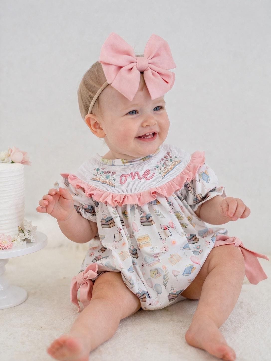 pink books flowers bows first birthday girl romper blush pink blue pastel floral and white outfit, pink and white smocked bubble romper first birthday chapter one books ruffle bows embroidered smocked long sleeve 1st birthday outfit romper baby girls, the mod mango, the mod mango baby co baby boutique