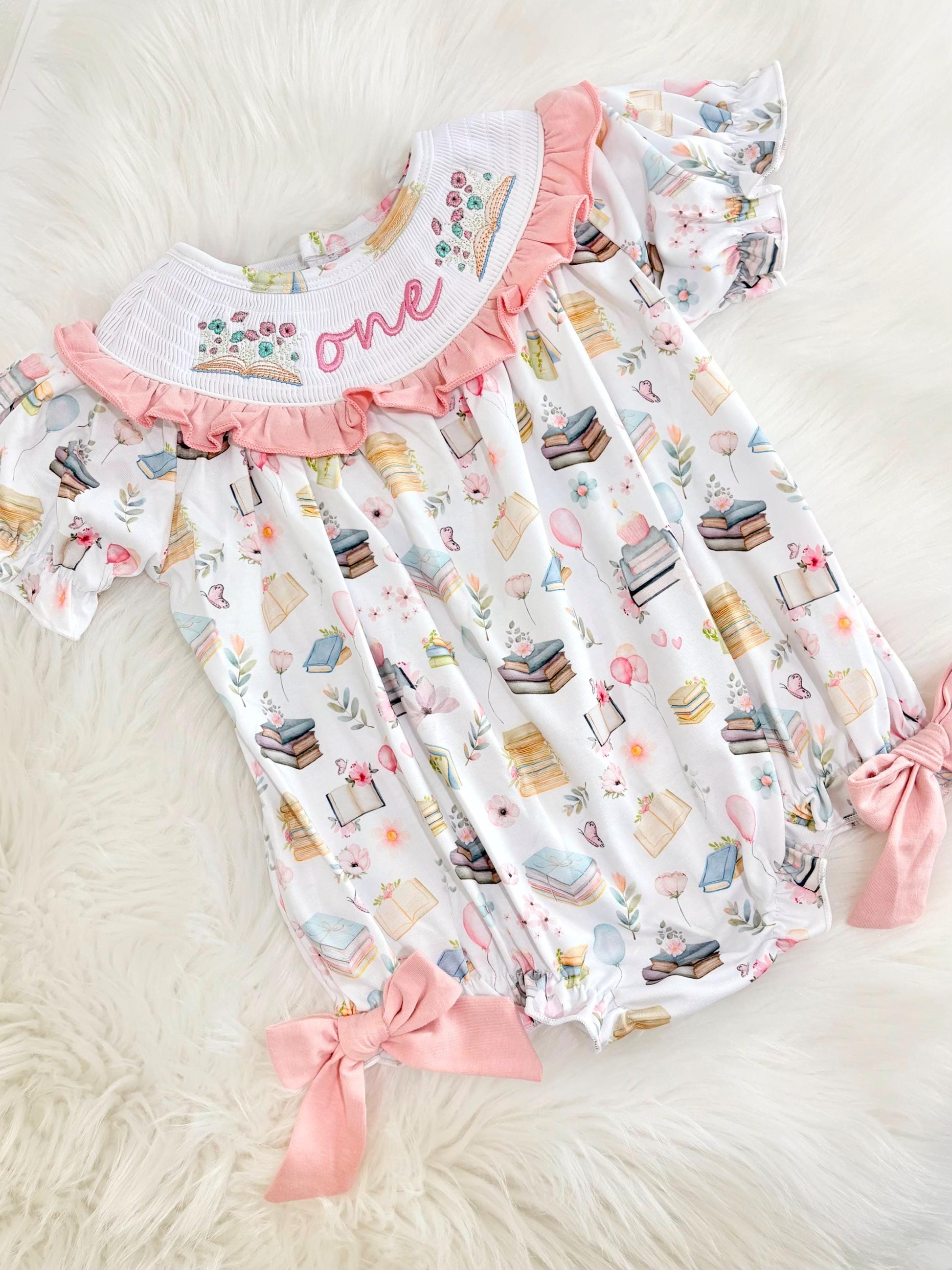 pink books flowers bows first birthday girl romper blush pink blue pastel floral and white outfit, pink and white smocked bubble romper first birthday chapter one books ruffle bows embroidered smocked long sleeve 1st birthday outfit romper baby girls, the mod mango, the mod mango baby co baby boutique